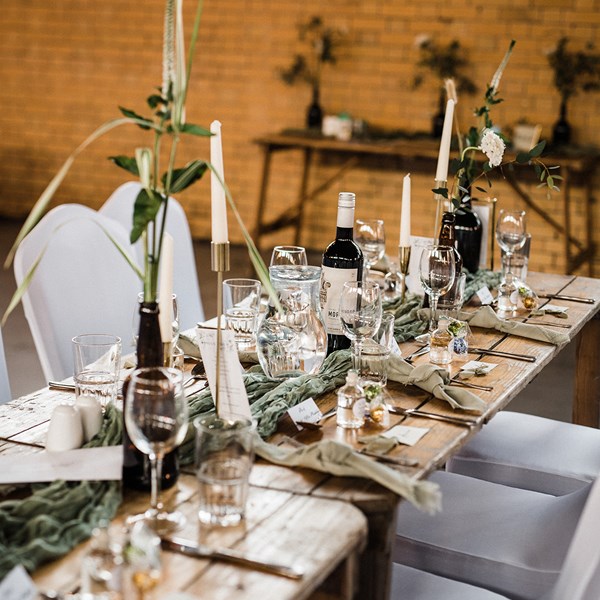 Wooden tables set for a wedding dinner decorated with foliage and candles.