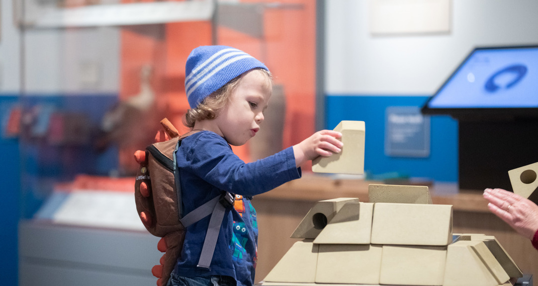 A child holding a white building brick in a museum gallery 