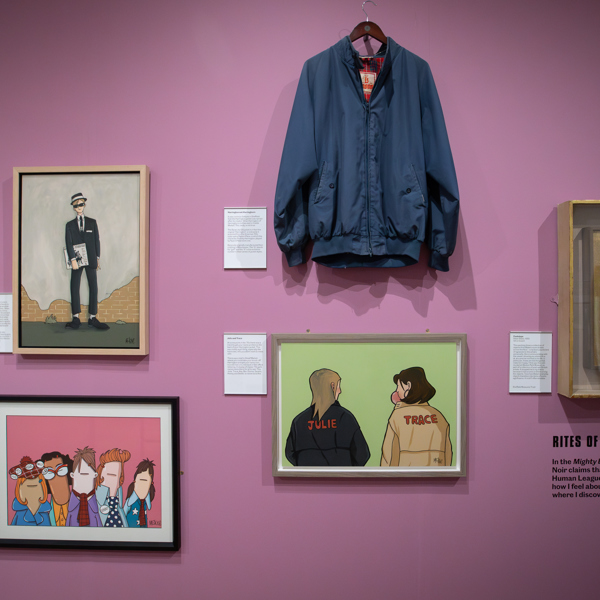 A group of colourful paintings and a 1970s harrington jacket displayed on a lilac wall in an art gallery 