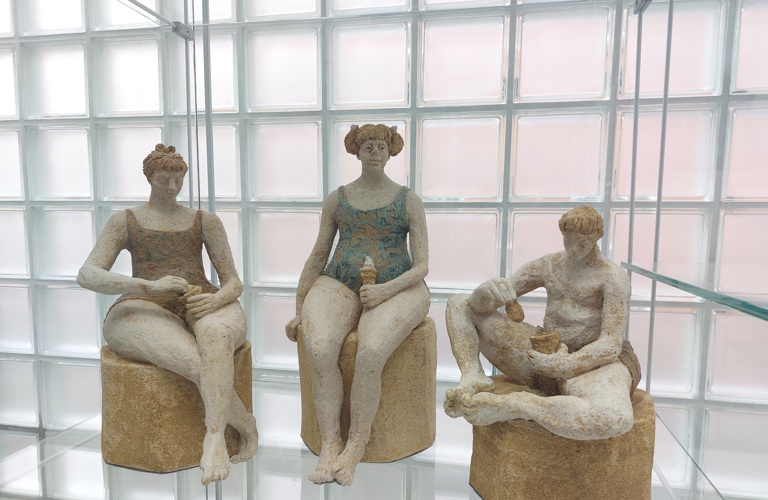 Three sculptures of two women and one man in swimming costumes eating ice creams. The colours are muted.