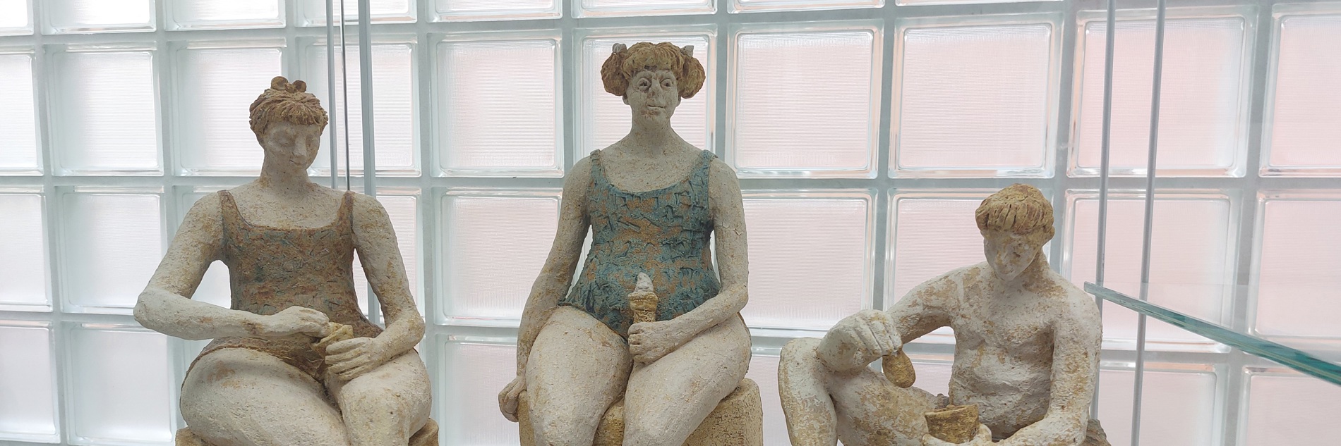 Three sculptures of two women and one man in swimming costumes eating ice creams. The colours are muted.