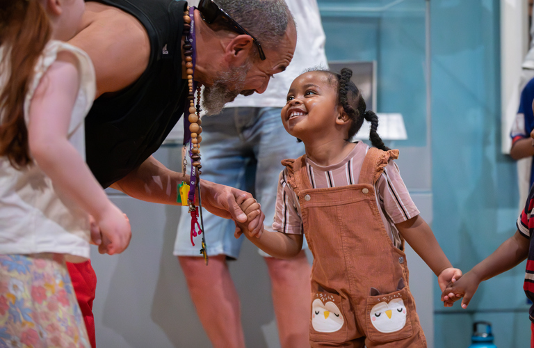 An adult and a child smiling at each other and holding hands in front of museum displays