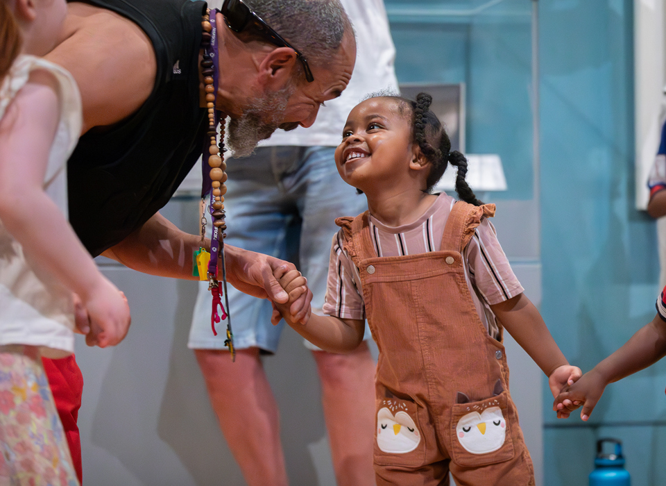 An adult and a child smiling at each other and holding hands in front of museum displays