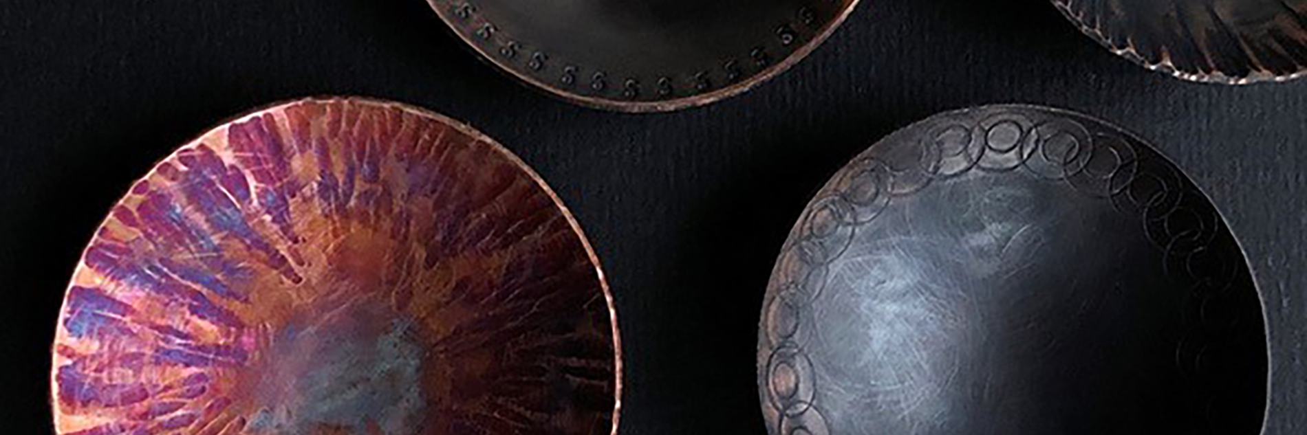 Four copper bowls. Three are dark grey with decorative details around the edges. One is orange and purple in colour.