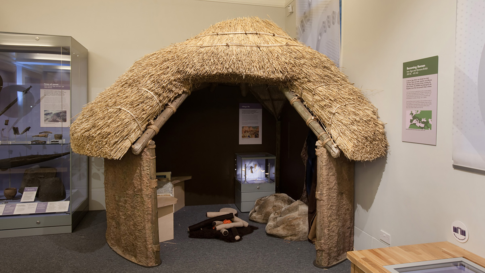 A thatched small round building with a large doorway through which you can see the interior including a replica camp fire. There are a couple of display cases inside and outside the roundhouse which hold artefacts and information sheets. 