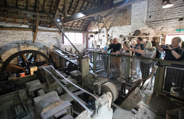 A group of adults looking at historical machinery in a grinding workshop. 