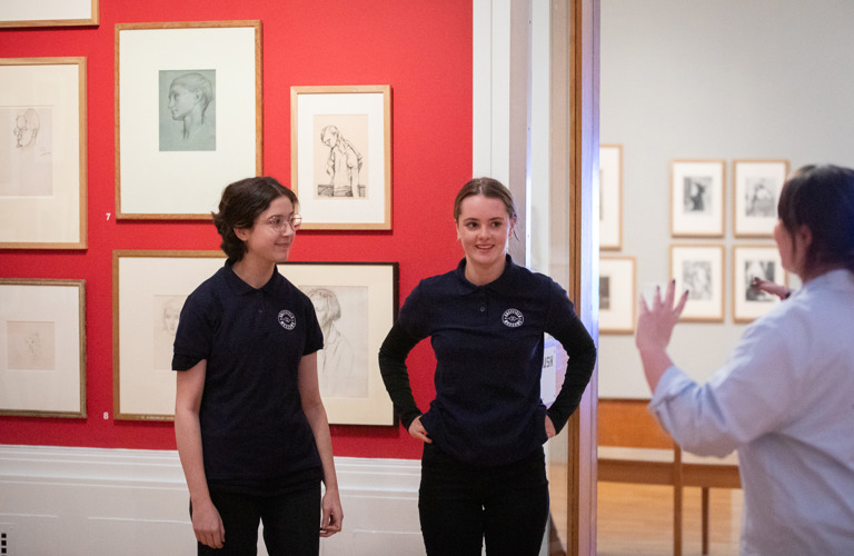 Two young people smile as they talk to an adult in a gallery setting.