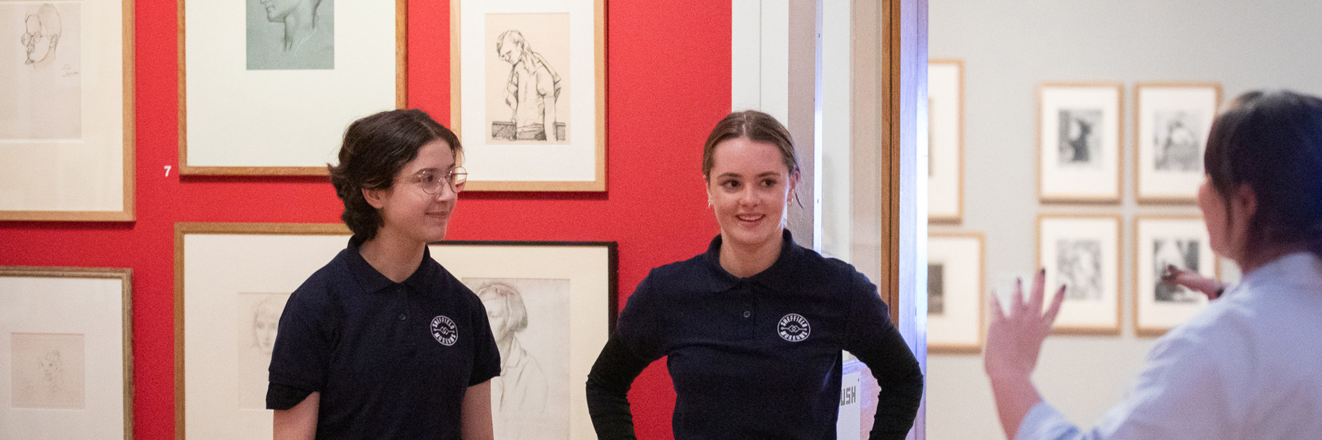 Two young people smile as they talk to an adult in a gallery setting.