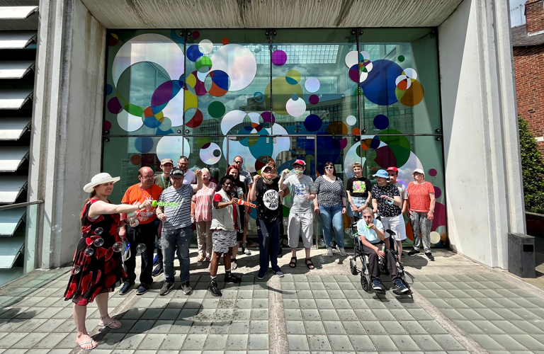 A group of adults in front of a large colourful artwork at the Millennium Gallery 