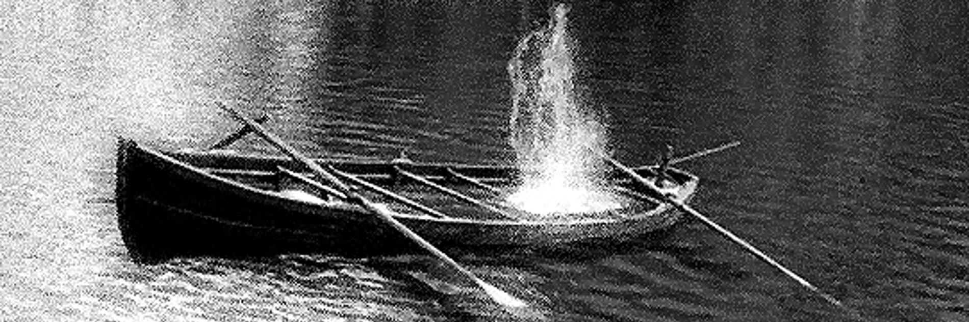 A black and white photograph of a canoe and oars in water.  