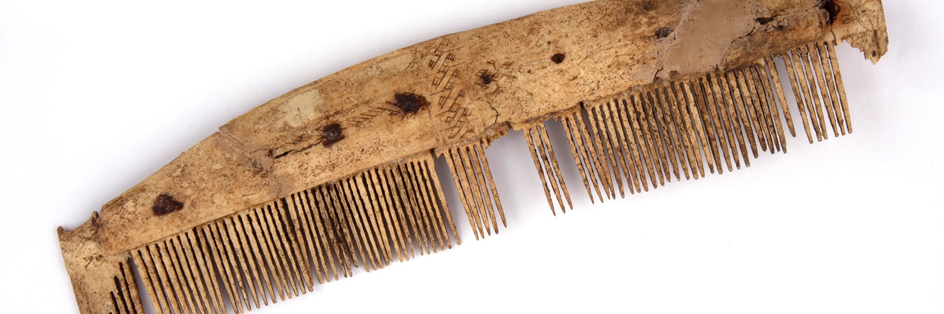 Remains of a light brown fine-toothed comb with decorative carving and some teeth missing.