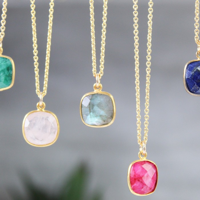A photograph of five necklaces crystal necklaces, all hanging on gold chains. The crystal colours from left to right are: green, pale pink, clear, bright pink and navy.