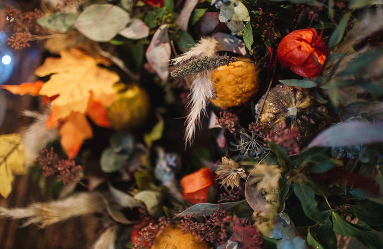A close-up of an autumnal bouquet made up of foliage and flowers in greens, yellows, oranges, purples and blues