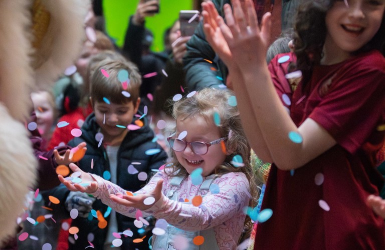 A photograph of three children celebrating with confetti in the air in front of them.