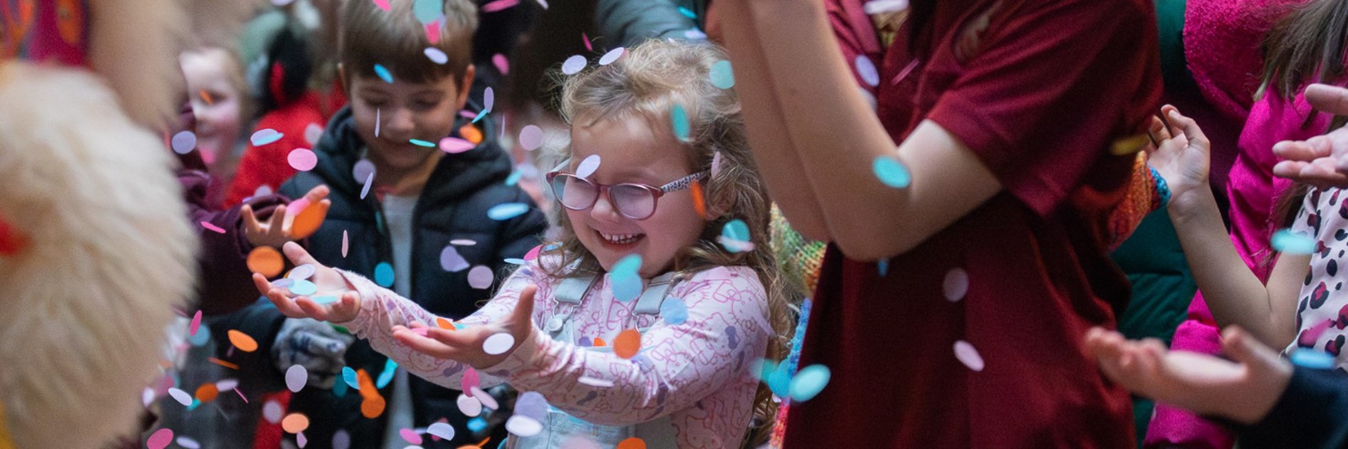 A photograph of three children celebrating with confetti in the air in front of them.