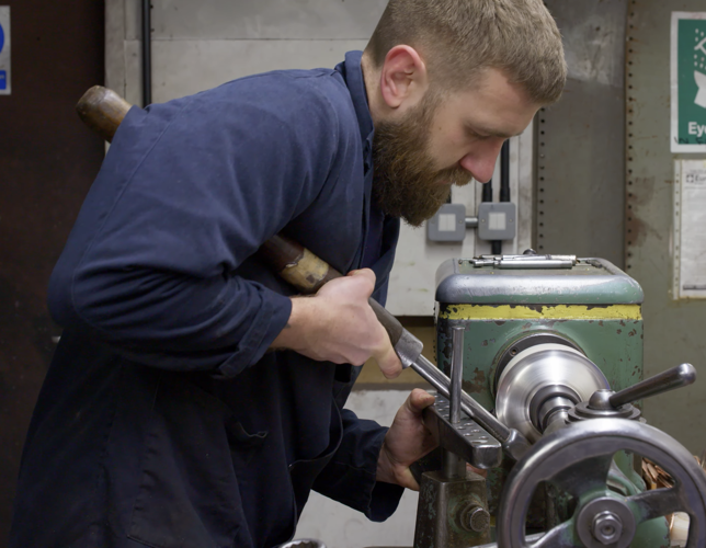 A photograph of an adult in a workshop using a piece of machinery. 