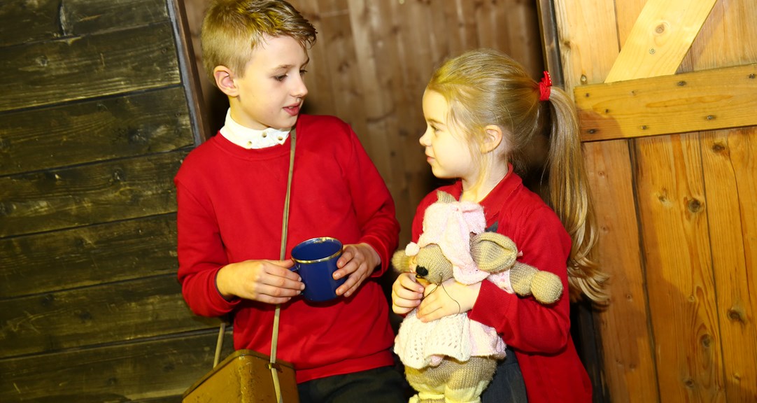 Two primary school age children, one holding a mug and the other a plush animal.
