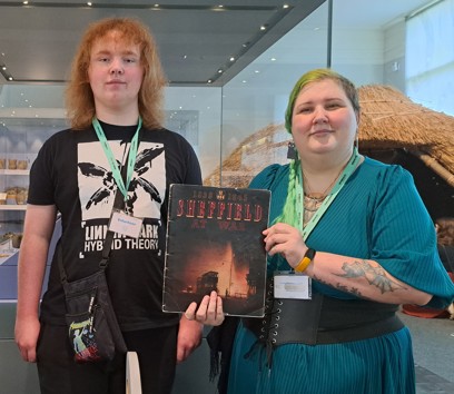 Two Museum volunteers standing in the Museum holding an old book about Sheffield to the camera.