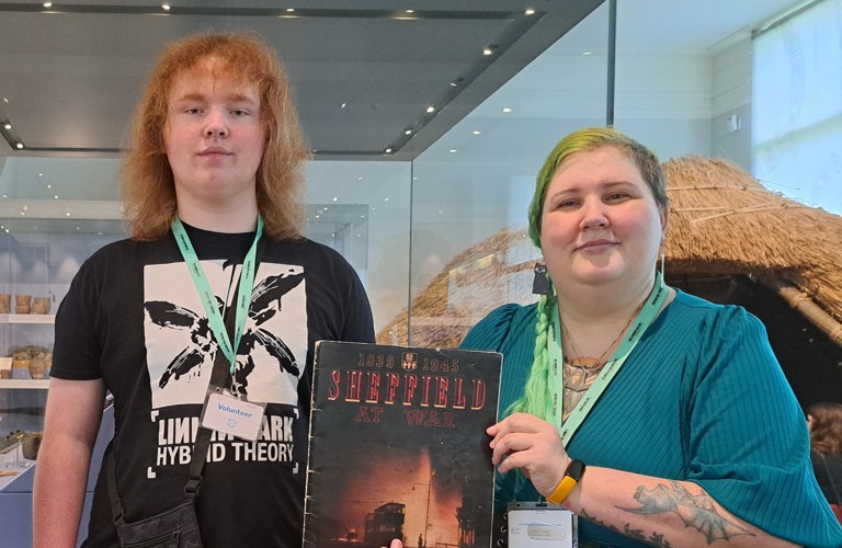 Two Museum volunteers standing in the Museum holding an old book about Sheffield to the camera.