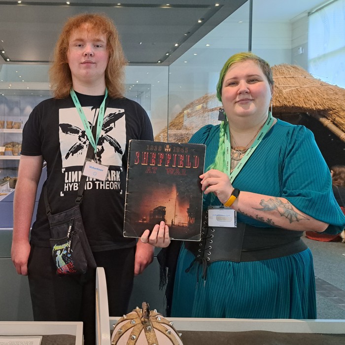 Two Museum volunteers standing in the Museum holding an old book about Sheffield to the camera.