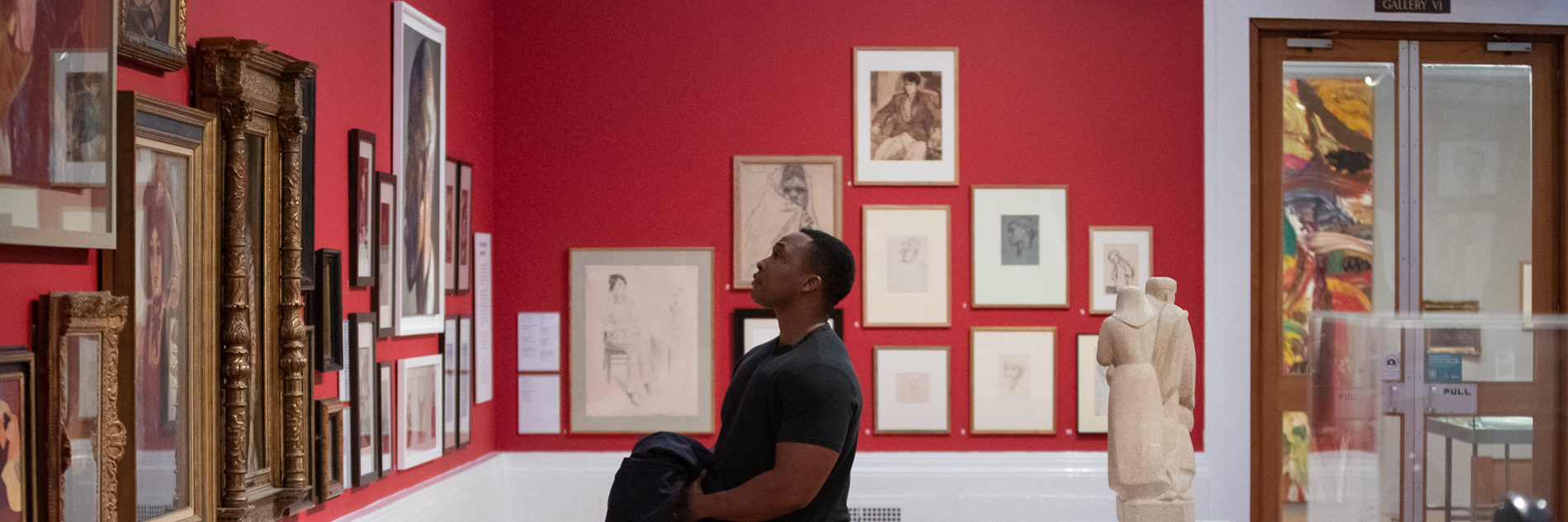 A visitor stands in Graves Gallery, looking at artworks on the red walls. 