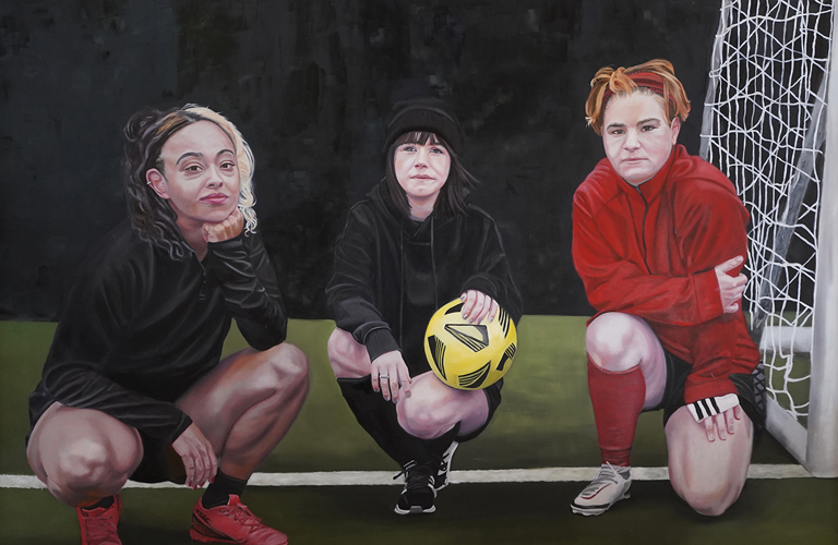 A painting of three teenage girls in football gear, all crouched next to the goal. The girl in the centre holds a yellow ball, all look directly out of the painting towards the viewer.