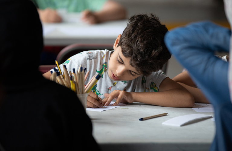 A child, sat at a table, drawing.
