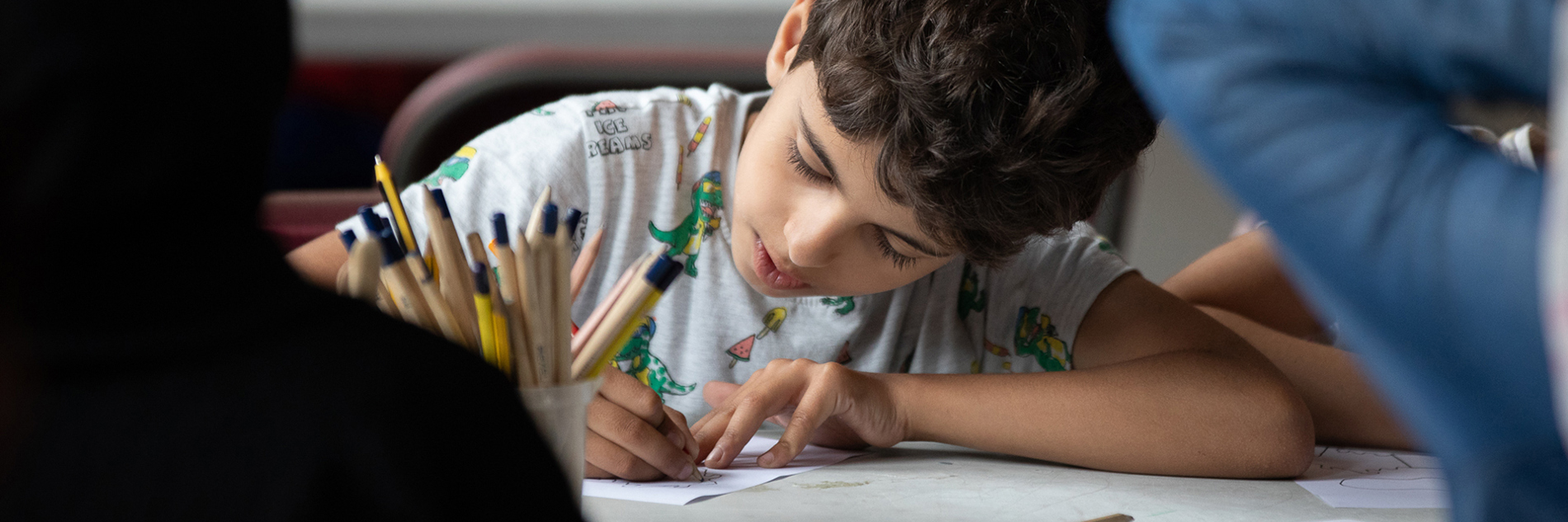 A child, sat at a table, drawing.