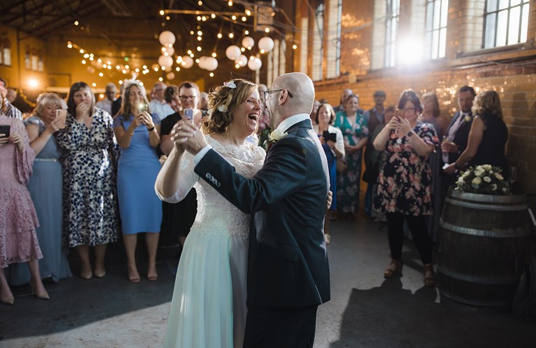 Two adults in wedding outfits dancing in front of a group of formally dressed adults  