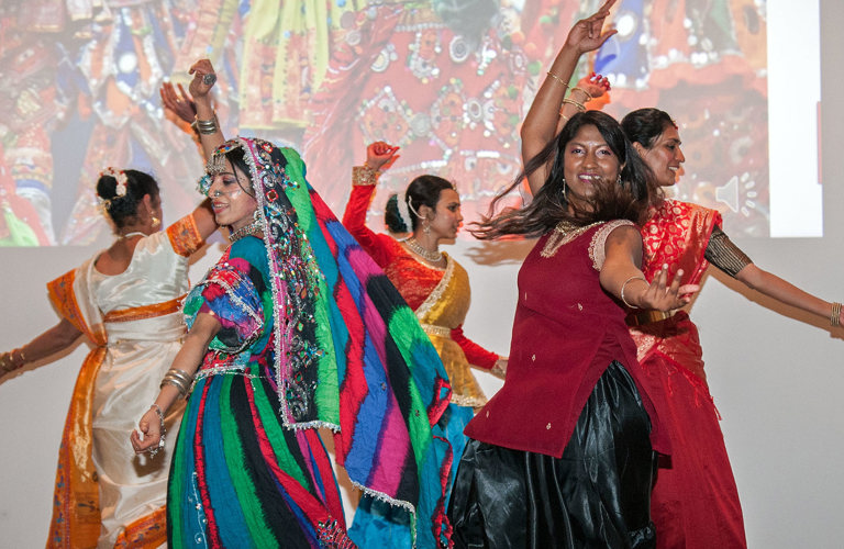 A group of adults dancing in a circle in South Asian traditional dress. 