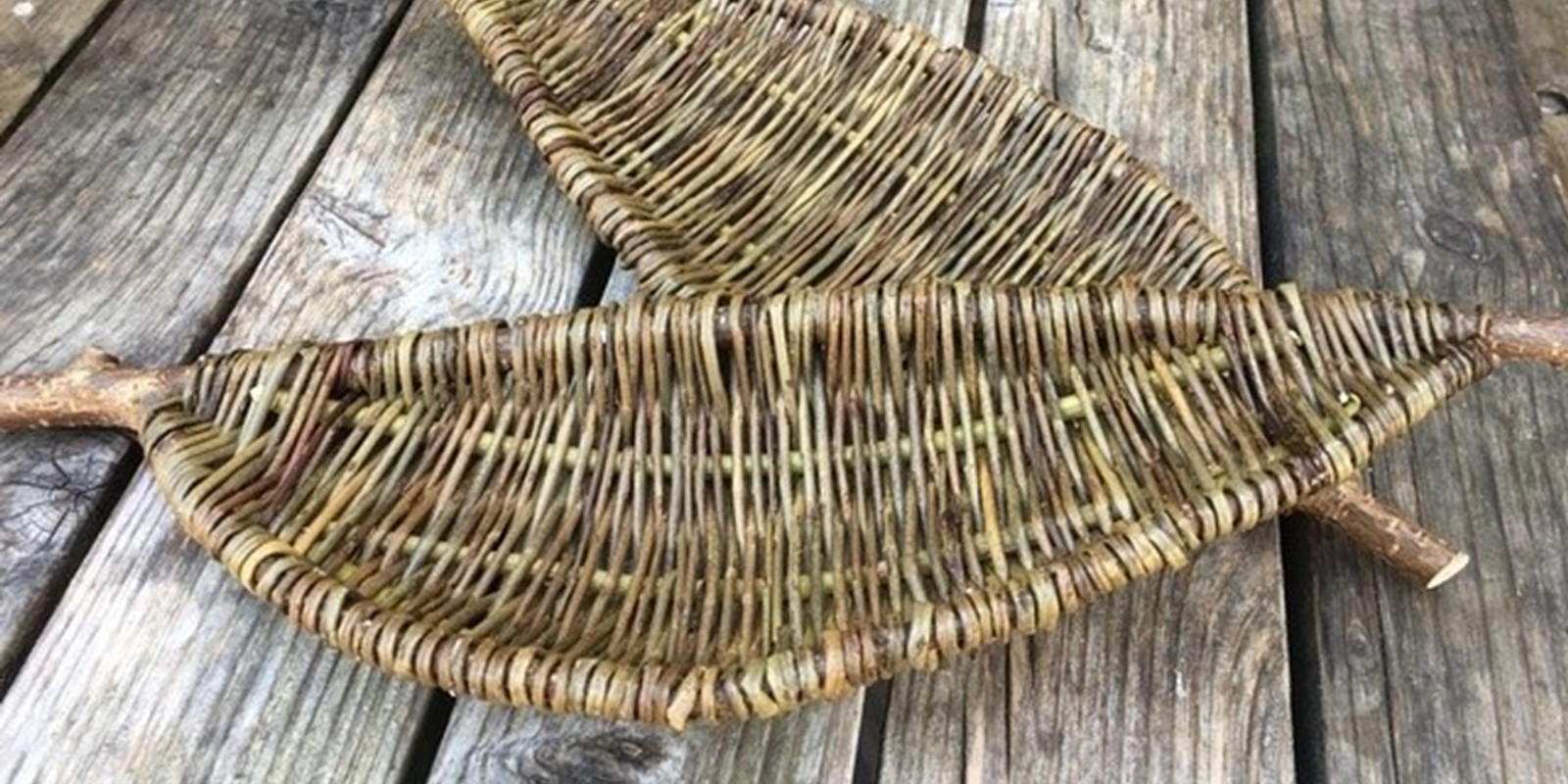 A photograph of two handwoven leaf shaped willow panels. They are placed on wooden slats.