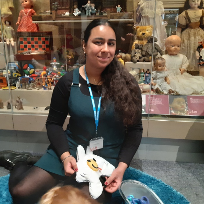 An adult sitting on a rug holding a child's toy in front of a display case of historic toys