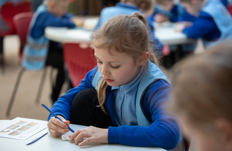 A child sitting at a table holding some clay and a modelling tool. 