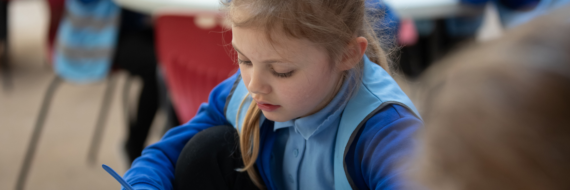 A child sitting at a table holding some clay and a modelling tool. 