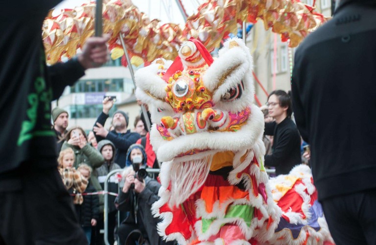 A photograph taken during a lion dance celebrating Chinese New Year. The head of a red, yellow and white dragon is visible.