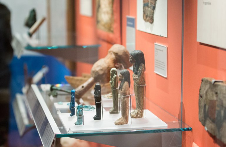 A gallery display case including several Ancient Egyptian sculptural artefacts depicting figures.