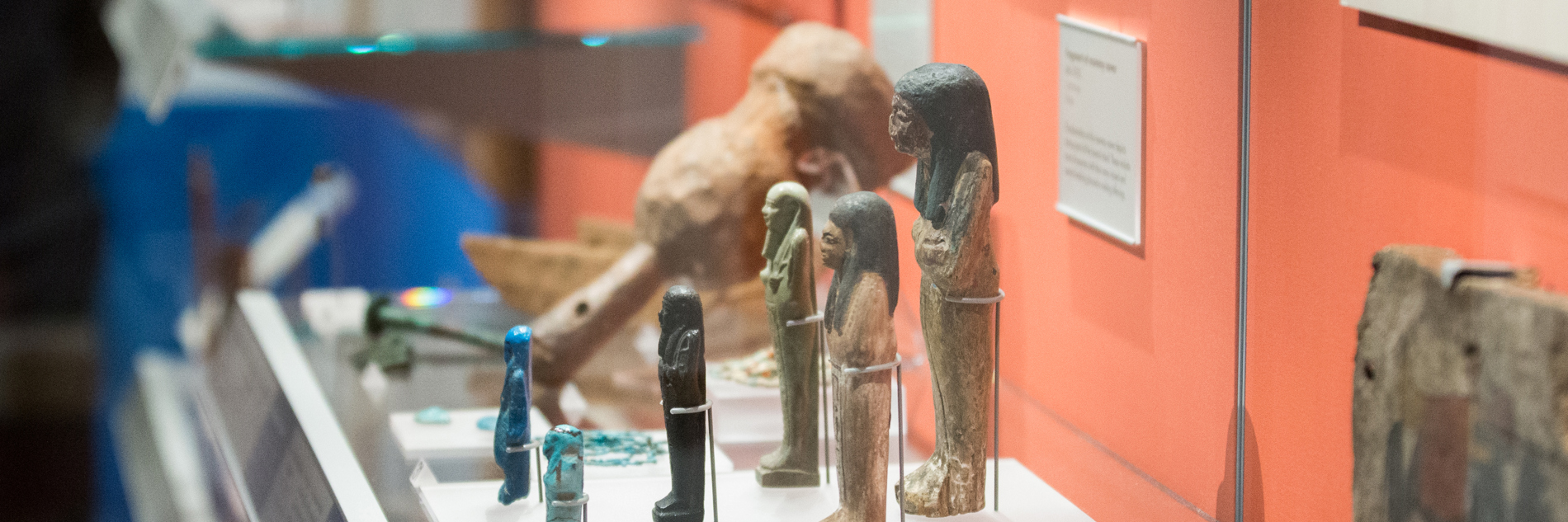 A gallery display case including several Ancient Egyptian sculptural artefacts depicting figures.