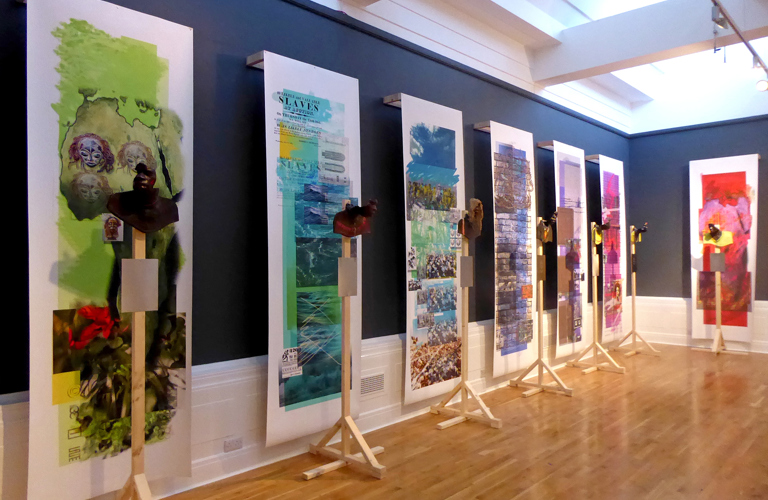 A series of seven hanging, horizontal colourful collages. Each collage has different images from faces to landscapes and brickwork. In front of each collage is a partial sculpture of a head 