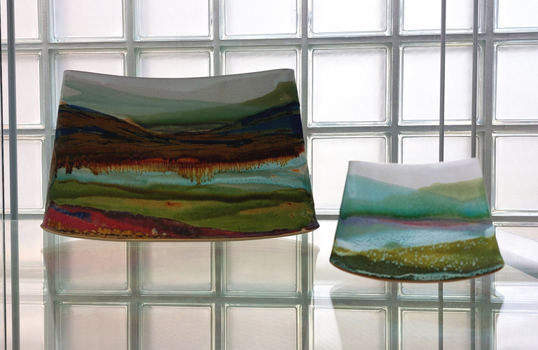 Landscape paintings painted on ceramics on display in a glass cabinet. 