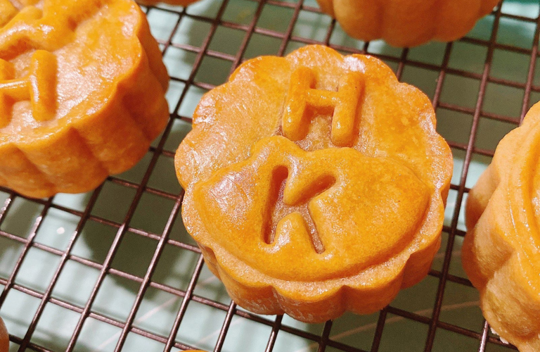 A series of baked pies each decorated with the letters H and K on a metal baking tray.