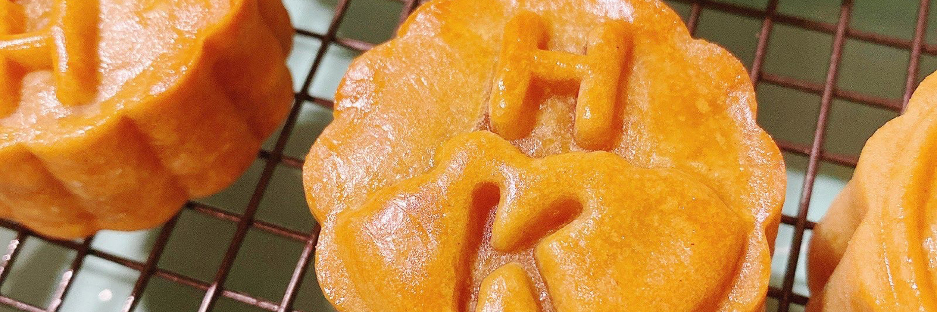 A series of baked pies each decorated with the letters H and K on a metal baking tray.