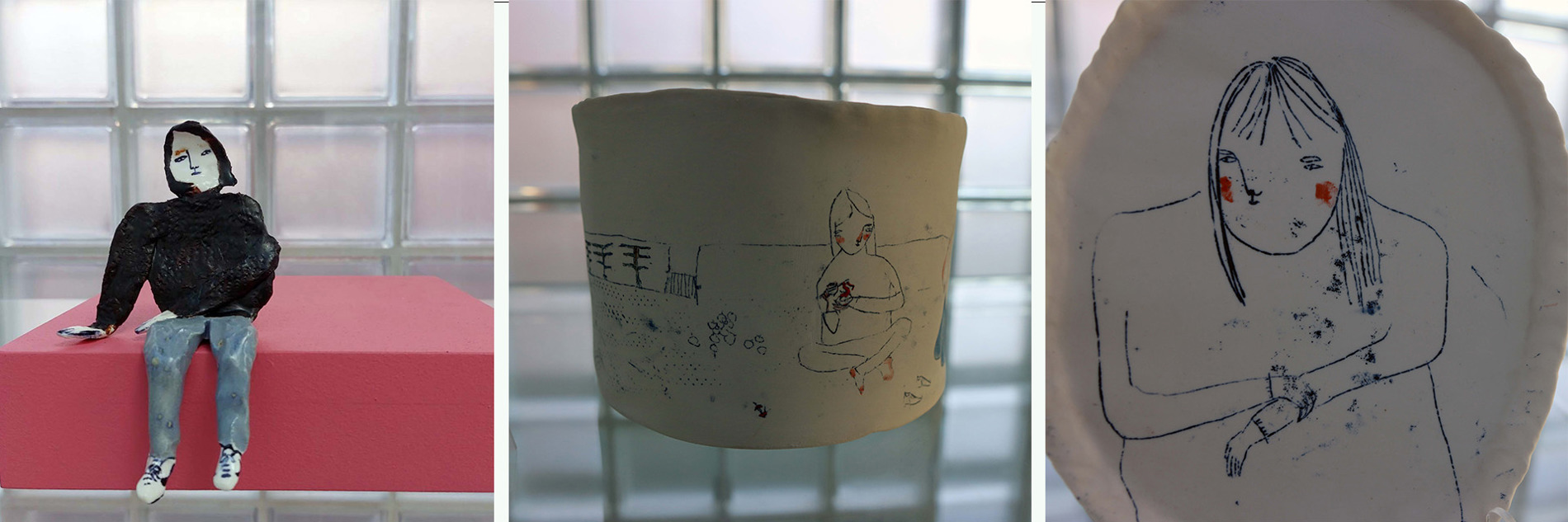 A ceramic sculpture of a figure sitting on a pink plinth, a white cylindrical vase and a drawing of a person on a ceramic plate.