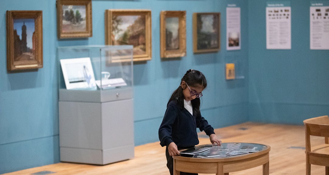 A primary school student leans over a table in a gallery with framed paintings on the walls. 