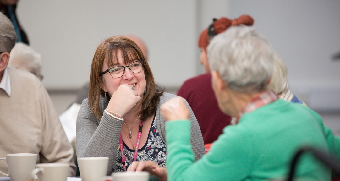 A group of adults talking, the one facing the camera is smiling. 