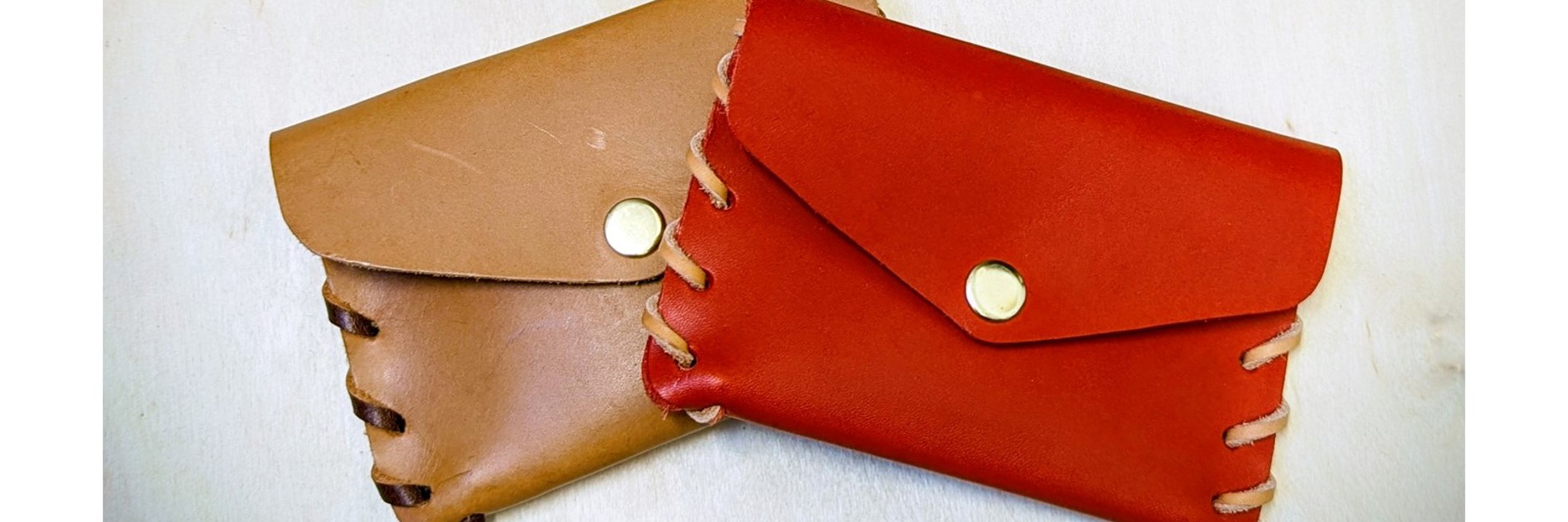 A photograph of two leather pouches, one is tan and the other is red. They are photographed against a white background.