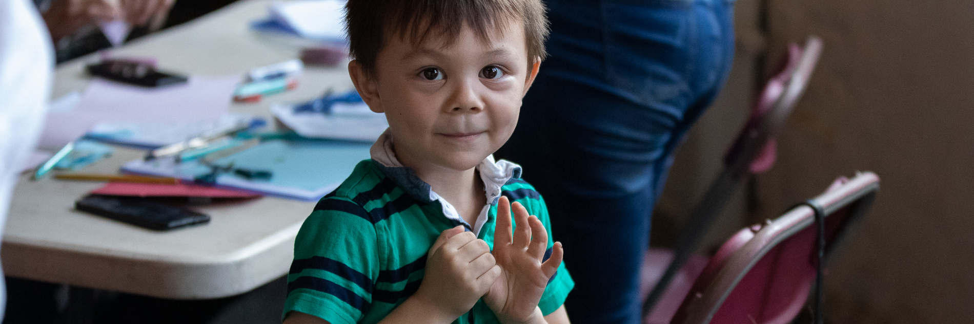 A photograph of a young boy waving at the camera.