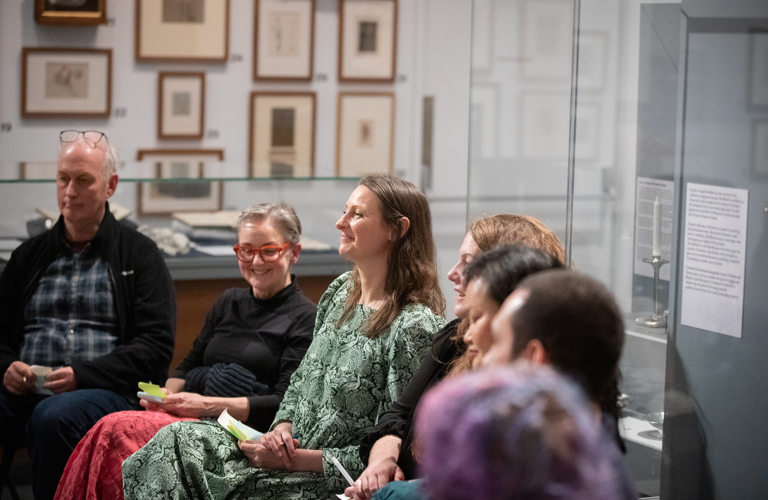 Group of people sitting on chairs in an art gallery. They're holding post-it notes and smiling.
