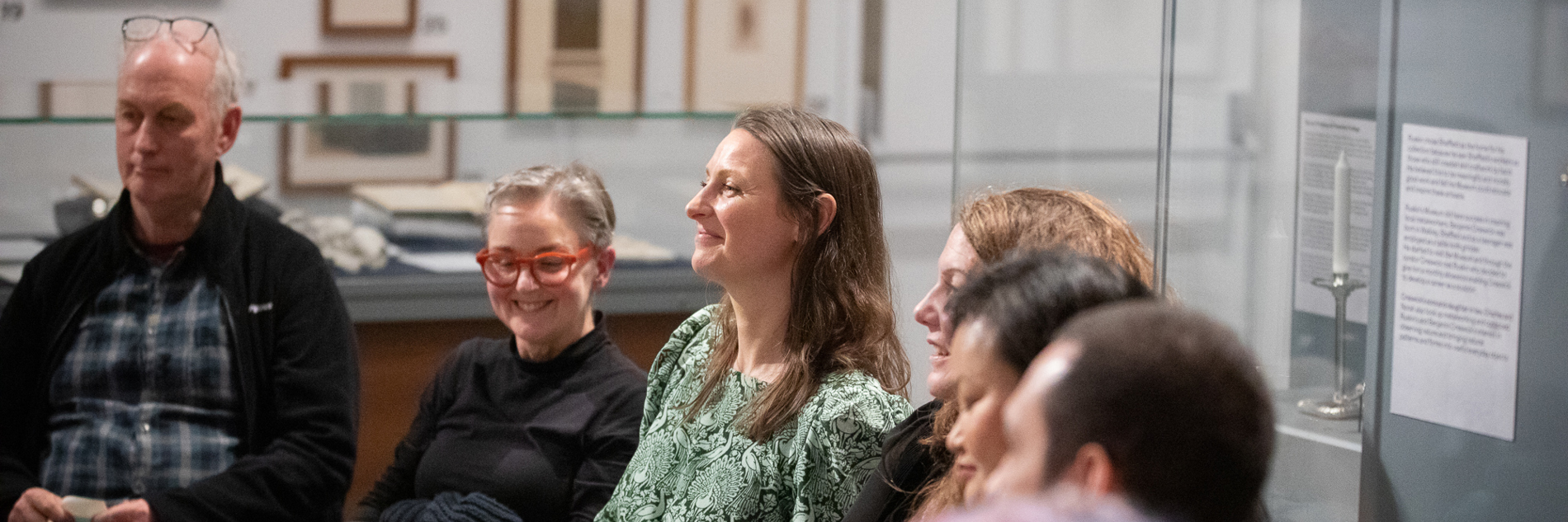 Group of people sitting on chairs in an art gallery. They're holding post-it notes and smiling.
